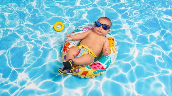 Bebê com oculos escuros deitado em bóia colorida na piscina