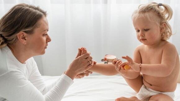 Uma mulher observa o pé de um bebê sentado à sua frente com um brinquedo nas mãos