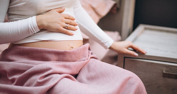 Mulher grávida sentada em uma cama tocando suavemente sua barriga