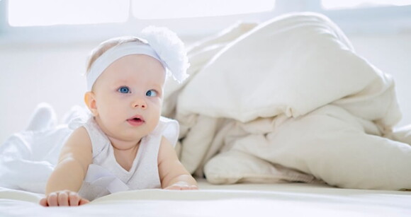 Imagem de bebê com estrabismo em cima da cama.