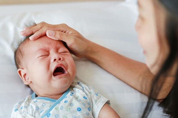 Imagem de um bebê com expressão de choro sendo acalmado pela mãe