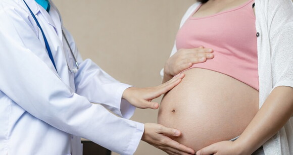 Imagem de um profissional da saúde colocando as mãos em cima da barriga de uma mulher grávida