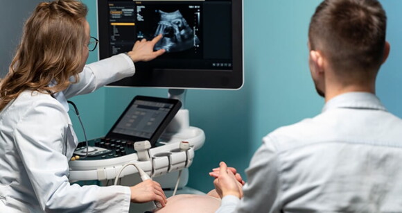 Imagem de uma médica realizando o exame de ultrassonografia em uma gestante
