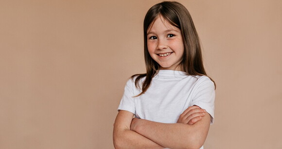 Menina de cabelo liso usando camiseta branca sorrindo com os braços cruzados