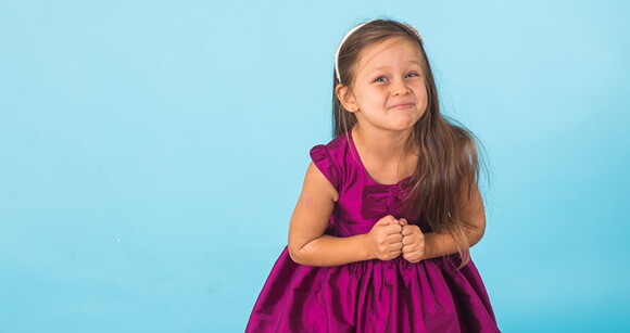 Menina usando vestido de princesa e tiara clara em frente a um fundo azul claro