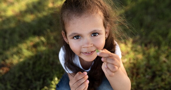 Menina de aproximadamente seis anos de cabelo escuro brincando na grama de um parque.