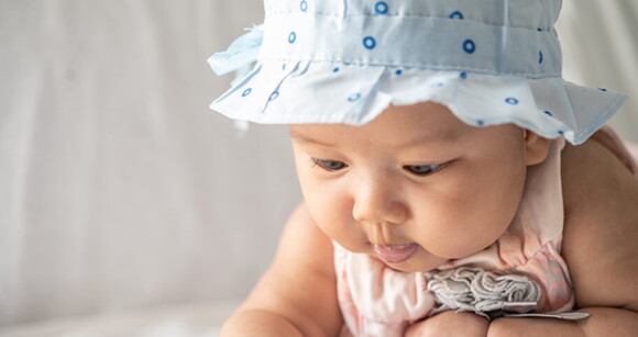 Bebê com roupa roupa e chapéu azul em um fundo branco e neutro