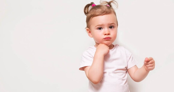 Menina de aproximadamente dois anos posando para a foto usando camiseta branca em um ambiente com fundo branco.