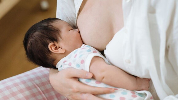 Um bebê recém-nascido deitado no colo de uma mulher sendo amamentado.