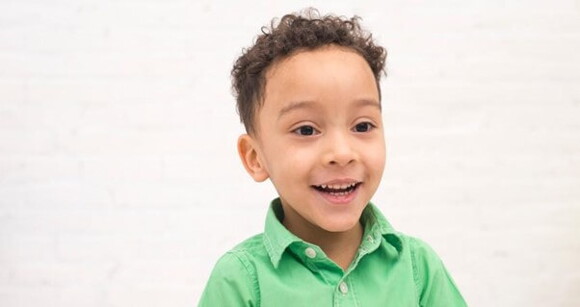 Menino de cabelo enrolado usando camisa verde sorrindo