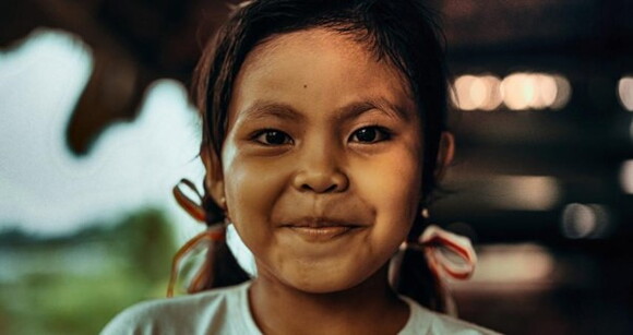 Menina de aproximadamente 6 anos com lacinhos no cabelo sorrindo timidamente