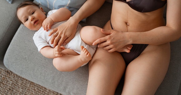 Mãe sentada no sofá ao lado do seu bebê usufruindo do conforto da calcinha pós-parto