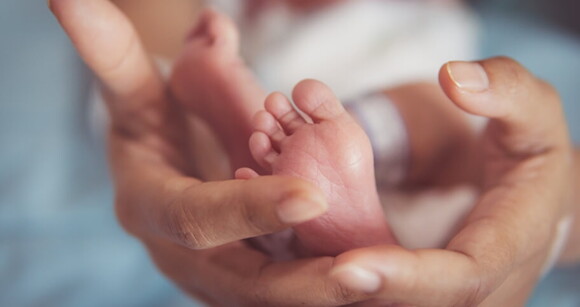 Mãos segurando delicadamente os pezinhos de um recém-nascido