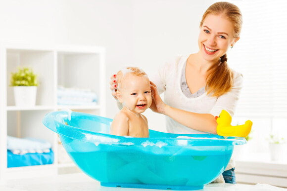mulher adulta dando banho em um bebê na banheira