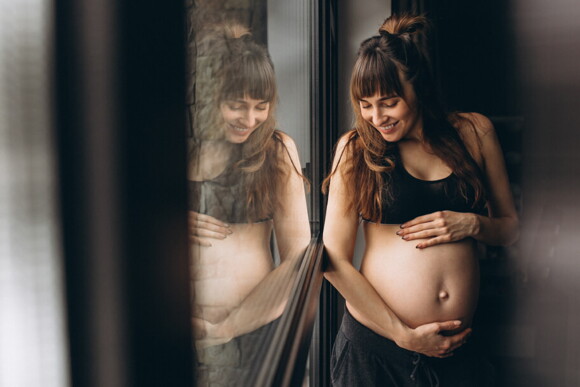 mulher grávida com as mãos na barriga e sorrindo
