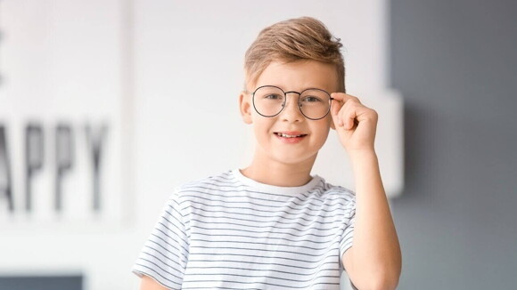 Menino com uma camiseta listrada, sorrindo e segurando a armação do óculos no rosto