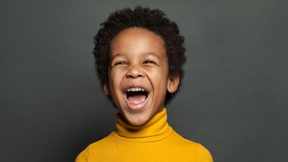 Menino sorridente e radiante vestindo uma blusa gola alta de cor amarela.