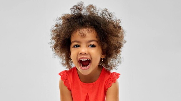 Menina sorridente de aproximadamente 4 anos de idade de cabelo crespo e roupa vermelha em um fundo claro.