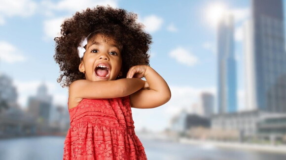 Menina com a boca aberta, vestindo um vestido vermelho com uma cidade ao fundo