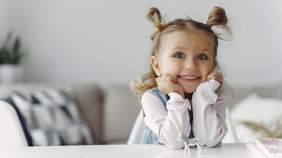 Menina sorrindo com os braços sobre a mesa apoiando o rosto