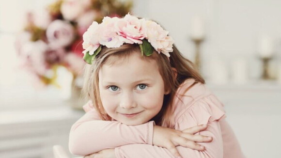 Menina com arco de flores na cabeça vestindo uma blusa rosa e olhando diretamente para a câmera.