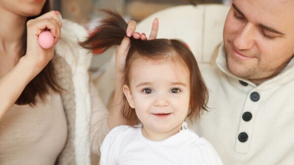 Uma mulher e um homem arrumando o cabelo de uma criança.