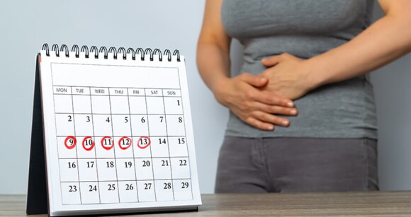 Imagem de calendário com dias riscados e mulher ao fundo com as duas mãos na barriga.