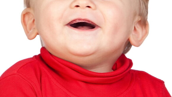 Close de um bebê sorridente, vestindo uma roupa vermelha, com uma expressão alegre deixando a gengiva à mostra.