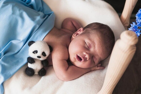 Recém-nascido do sexo masculino dormindo em uma superficie aconchegante com um mini urso panda do seu  lado