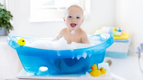 Bebê em uma banheira infantil cheia de espuma, com patos de borracha à sua volta.