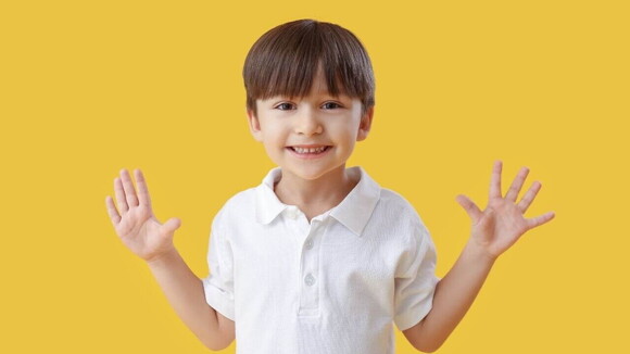 Menino sorrindo com as mãos abertas, sobre um fundo amarelo