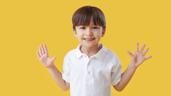 Menino sorrindo com as mãos abertas sobre um fundo amarelo