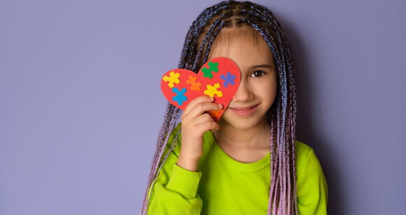 Imagem de uma menina segurando um coração de papel com desenho de quebra-cabeça, representa a complexidade e a diversidade do Transtorno do Espectro Autista