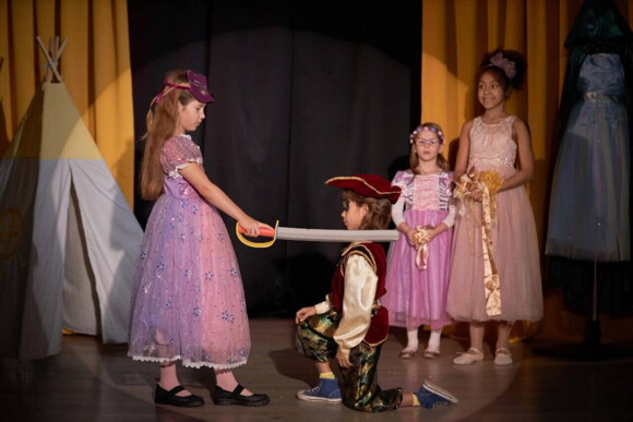 Grupo de crianças em cima de um palco, atuando em uma peça de teatro infantil.