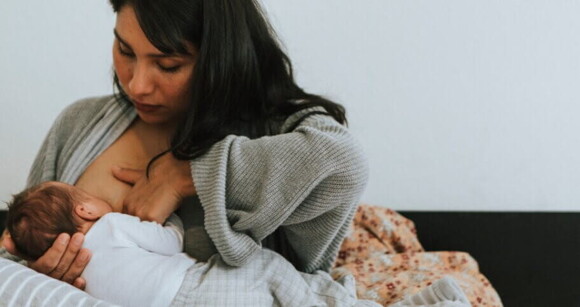 Mulher amamentando bebê recém-nascido na cama