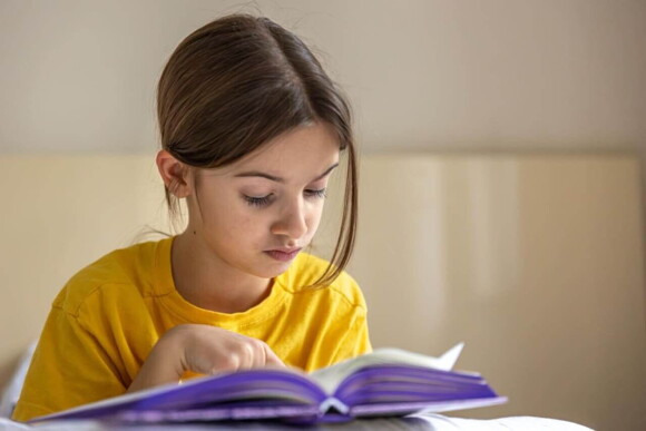 Uma menina sentada e com feição de concentração, lendo um livro.