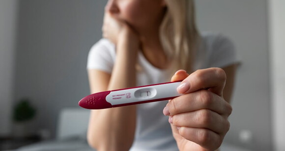 Mulher aflita segurando um teste de grávidez de farmácia com resultado negativo